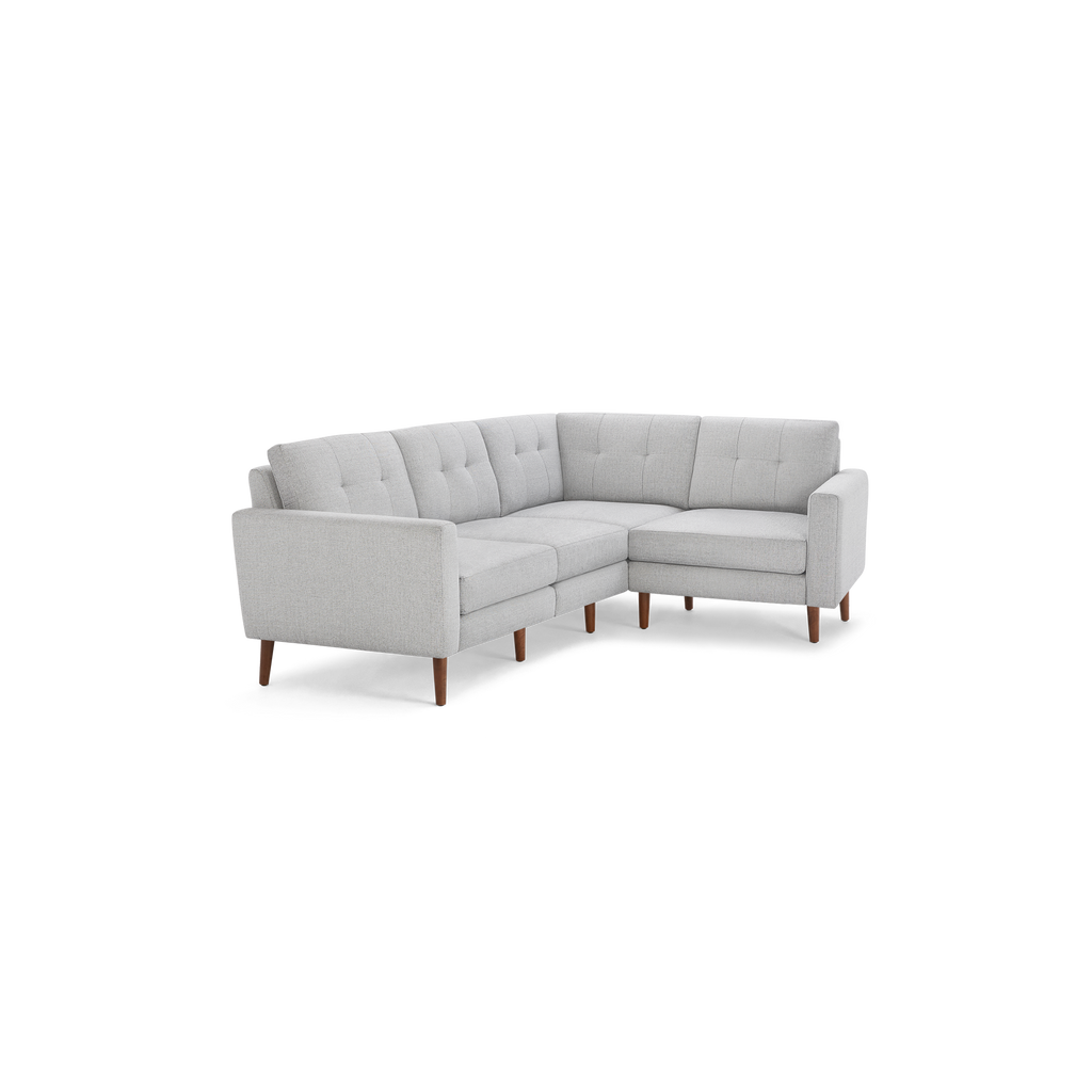 Light gray fabric upholstered sectional sofa with tufted back cushions and wooden legs, designed for corner placement.