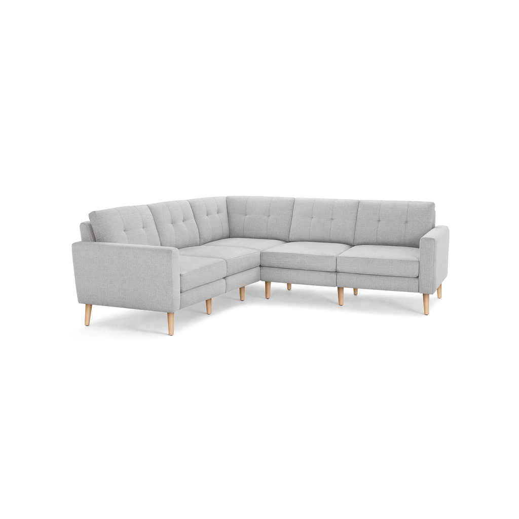 Light gray L-shaped sectional sofa with tufted back cushions and wooden tapered legs on black background.
