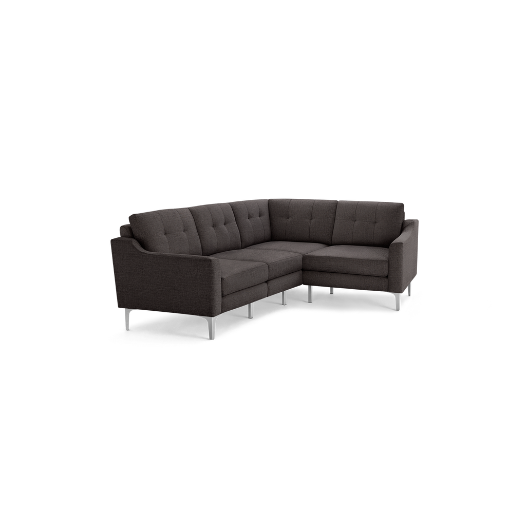 Dark gray modern L-shaped sectional sofa with tufted cushions and slim silver metal legs isolated on black background.