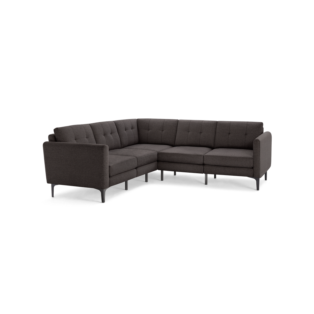 Dark gray L-shaped sectional sofa with tufted cushions, slim armrests, and modern black legs, isolated on black background.