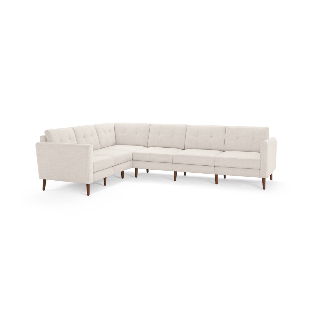 Large L-shaped sectional sofa in light beige fabric with tufted back cushions and wooden legs, designed for spacious living rooms.