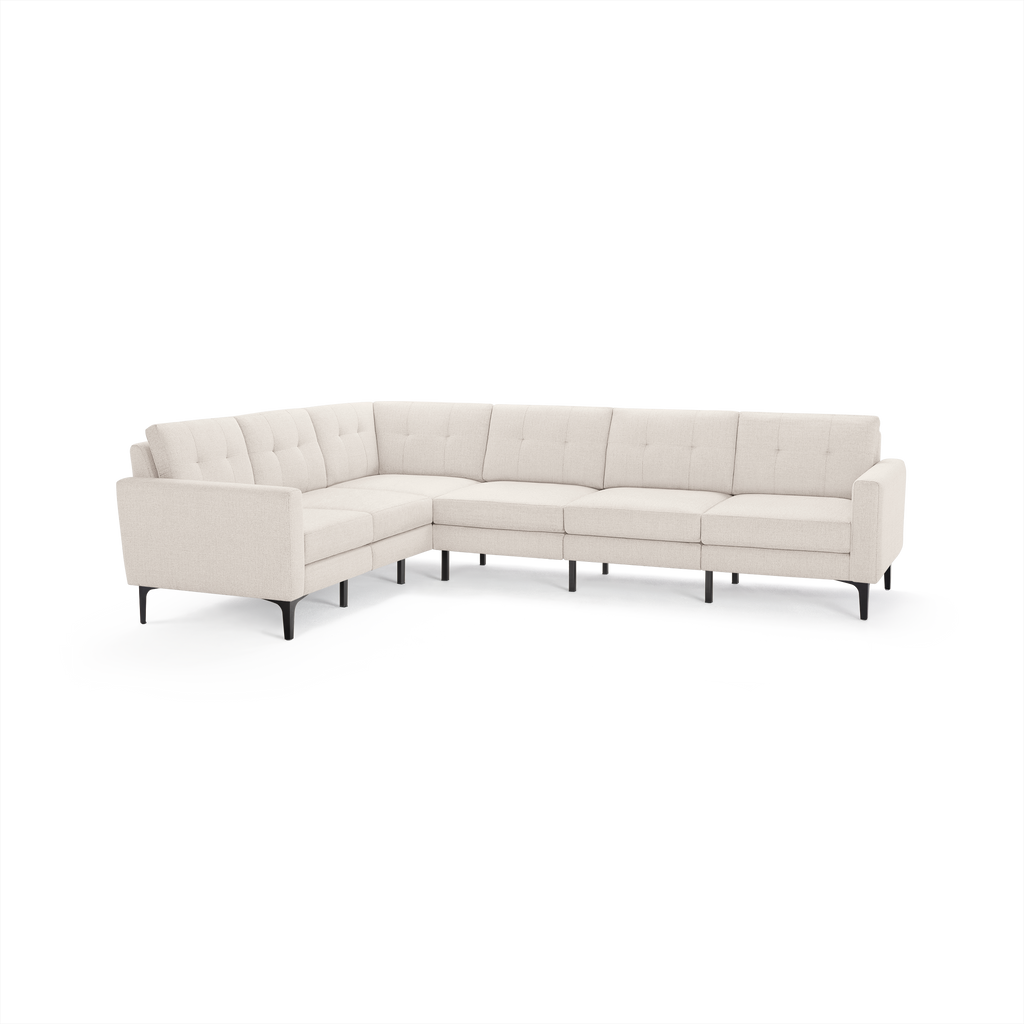 Large modern L-shaped sectional sofa with beige fabric upholstery, tufted back cushions, and slim angled black legs.