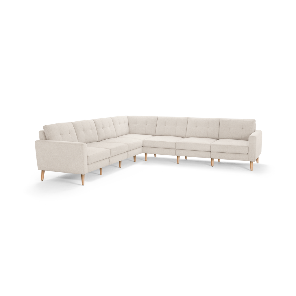 Large L-shaped sectional sofa with beige tufted fabric upholstery, clean lines, and light wooden tapered legs.