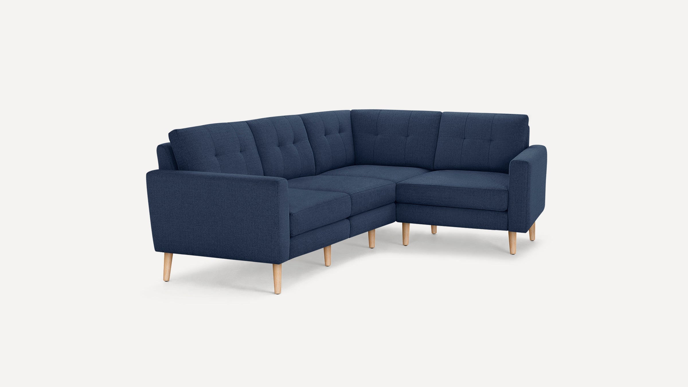 Modern L-shaped navy blue fabric sofa with tufted back cushions and light wooden legs, set against a white background.