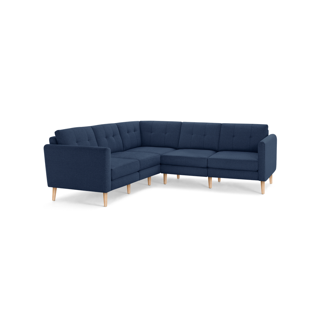 Modern L-shaped sectional sofa with navy blue tufted fabric upholstery and light wooden legs on a black background.