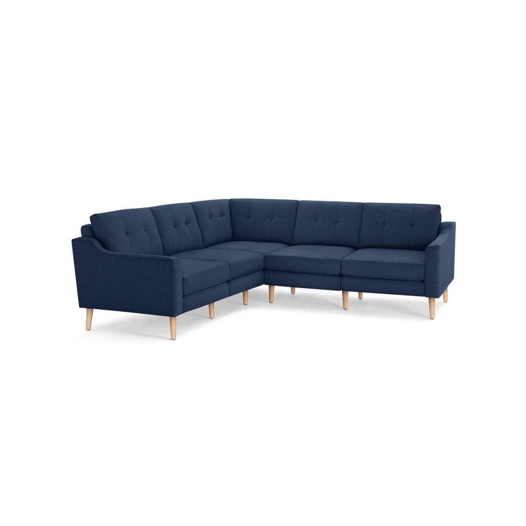 L-shaped sectional sofa with tufted navy blue fabric cushions and light wooden legs, featuring clean lines and mid-century modern design.