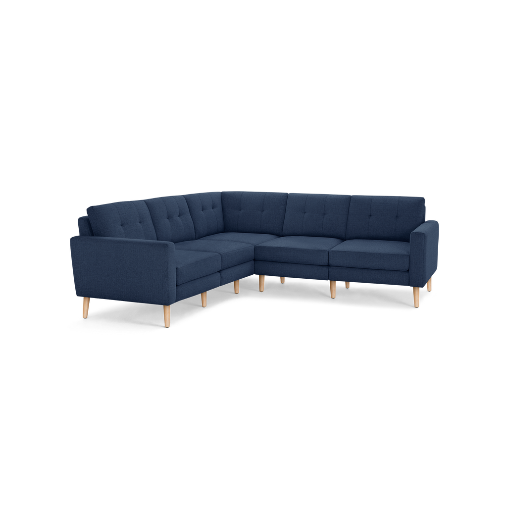 L-shaped sectional sofa in navy blue fabric with tufted back cushions and light wooden legs, designed for modern living spaces.