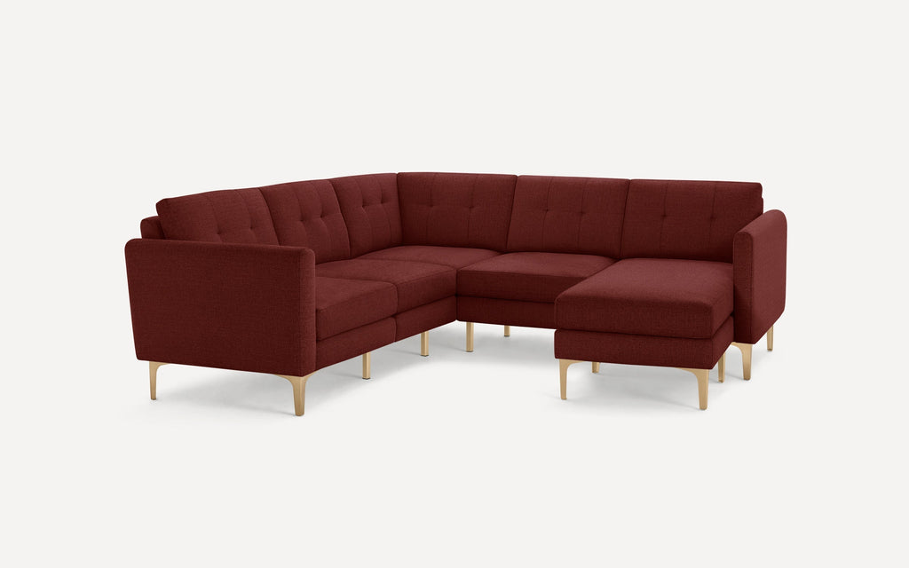 Modern L-shaped sectional sofa in deep red fabric with tufted cushions and sleek light wooden legs on white background.
