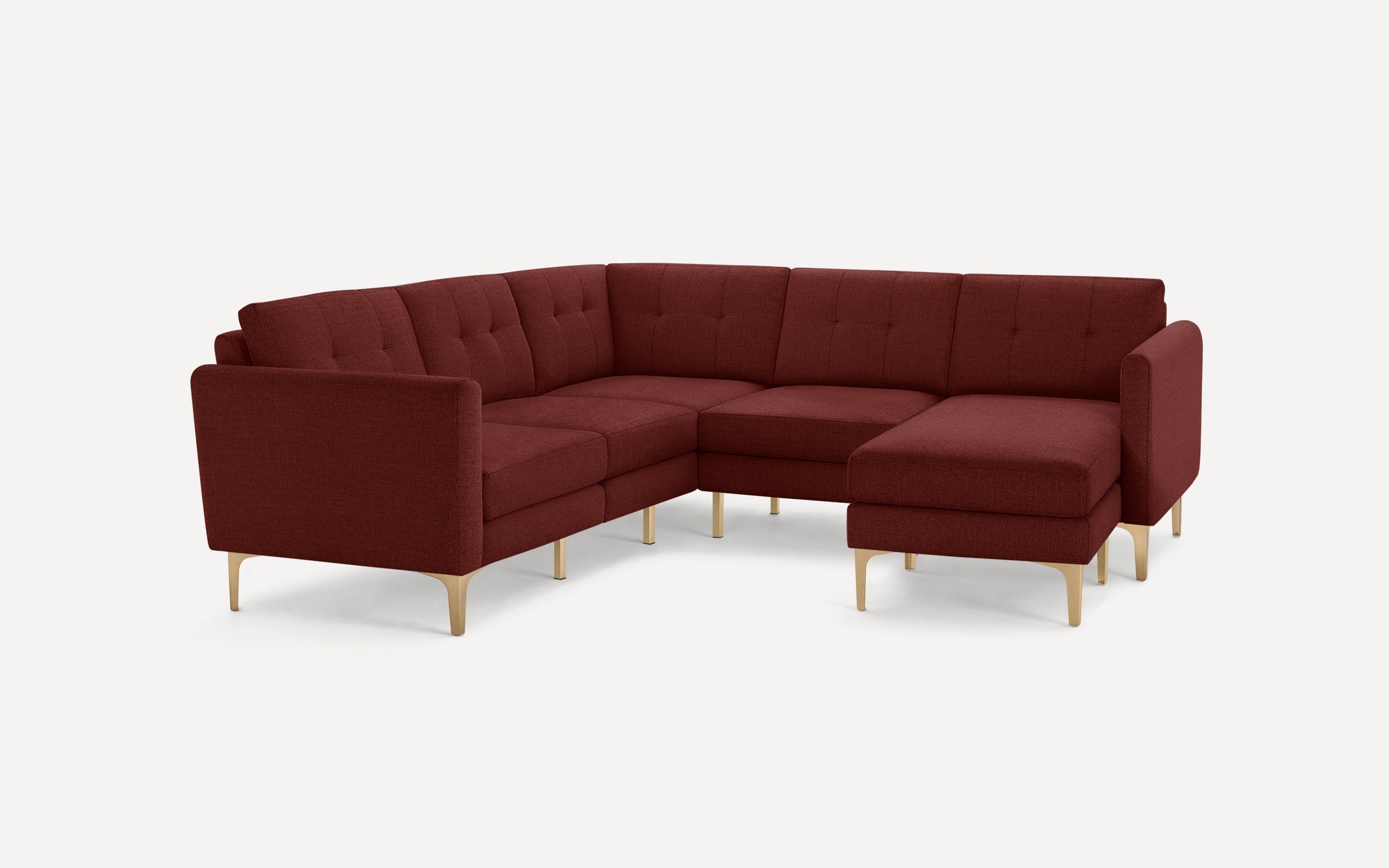 Modern L-shaped sectional sofa in deep red fabric with tufted cushions and sleek light wooden legs on white background.