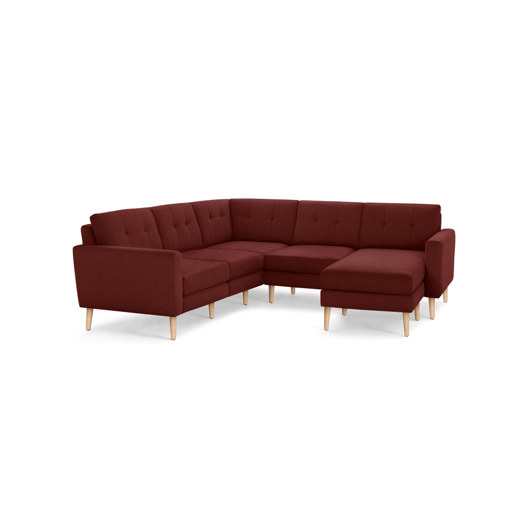 L-shaped sectional sofa in dark red fabric with button-tufted back cushions and light wooden legs, featuring a chaise lounge on the right side.
