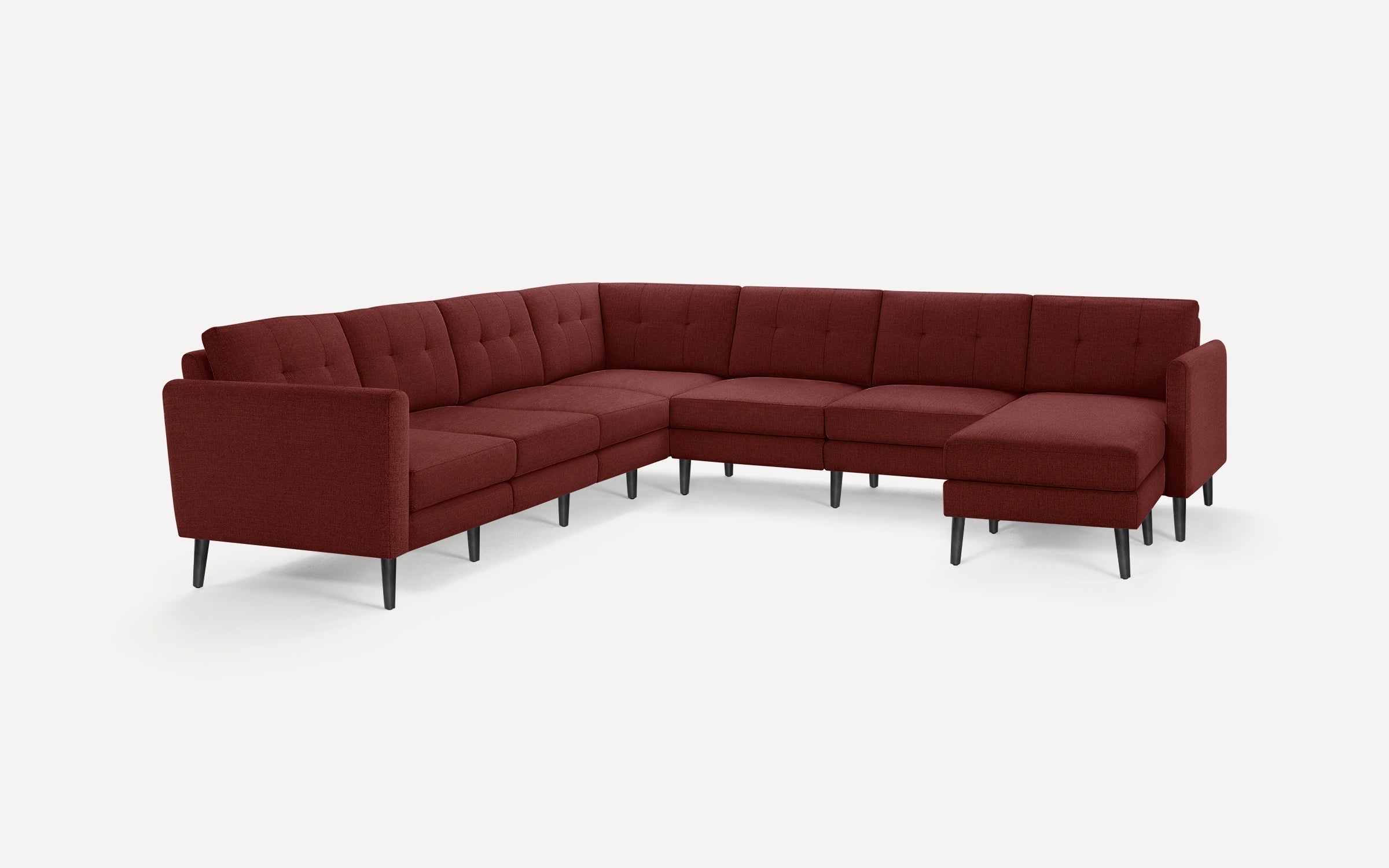 Large modern L-shaped sectional sofa in deep burgundy fabric with tufted back cushions and black tapered legs, isolated on white background.