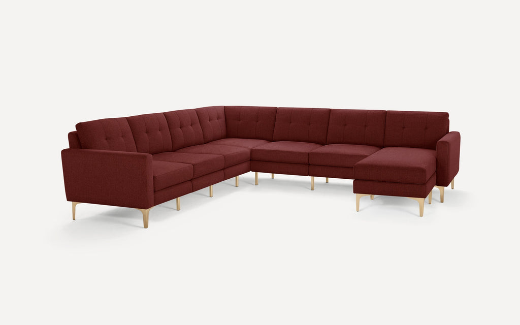 Modern L-shaped sectional sofa with tufted back cushions, deep burgundy fabric upholstery, and light wooden tapered legs, isolated on white background.