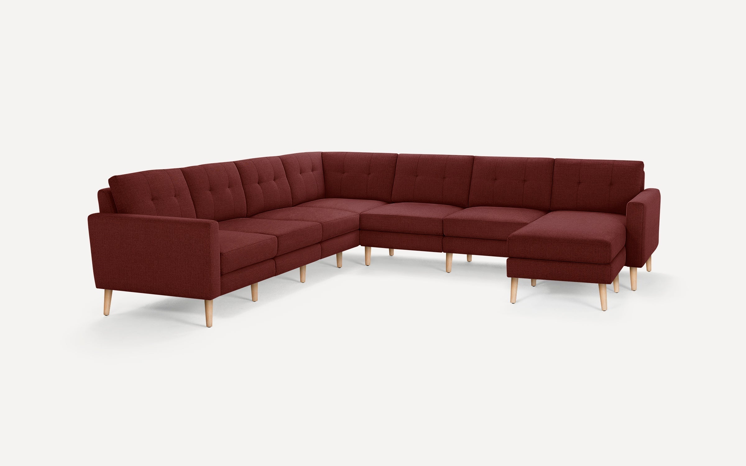Large modern L-shaped sectional sofa in deep burgundy fabric with tufted back cushions and light wooden legs against white background.