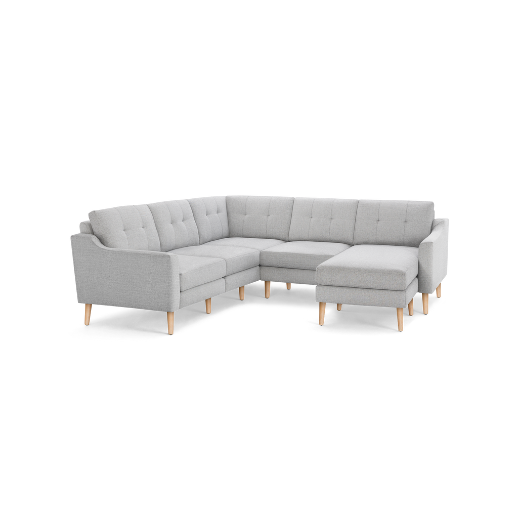 Light gray fabric L-shaped sectional sofa with tufted back cushions and wooden legs, featuring a chaise lounge on the right side.