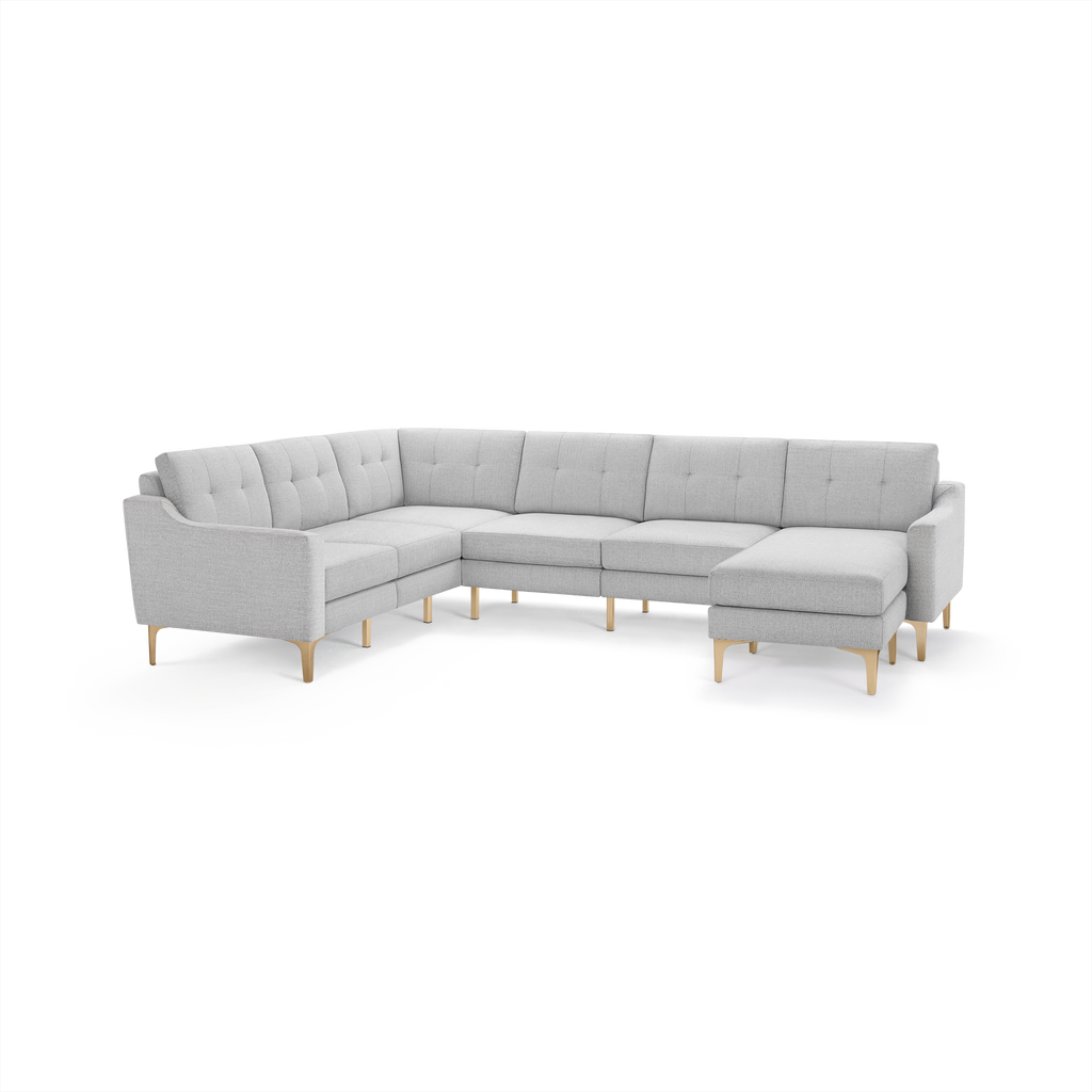 Light gray fabric sectional sofa with L-shape design, tufted back cushions, slim wooden legs, and a chaise lounge on the right side.