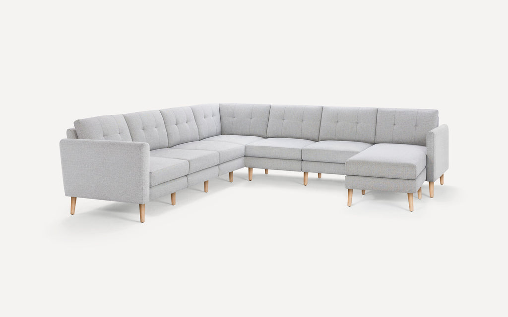 Light gray fabric upholstered sectional sofa with tufted back cushions and wooden legs, featuring a chaise lounge on the right side.