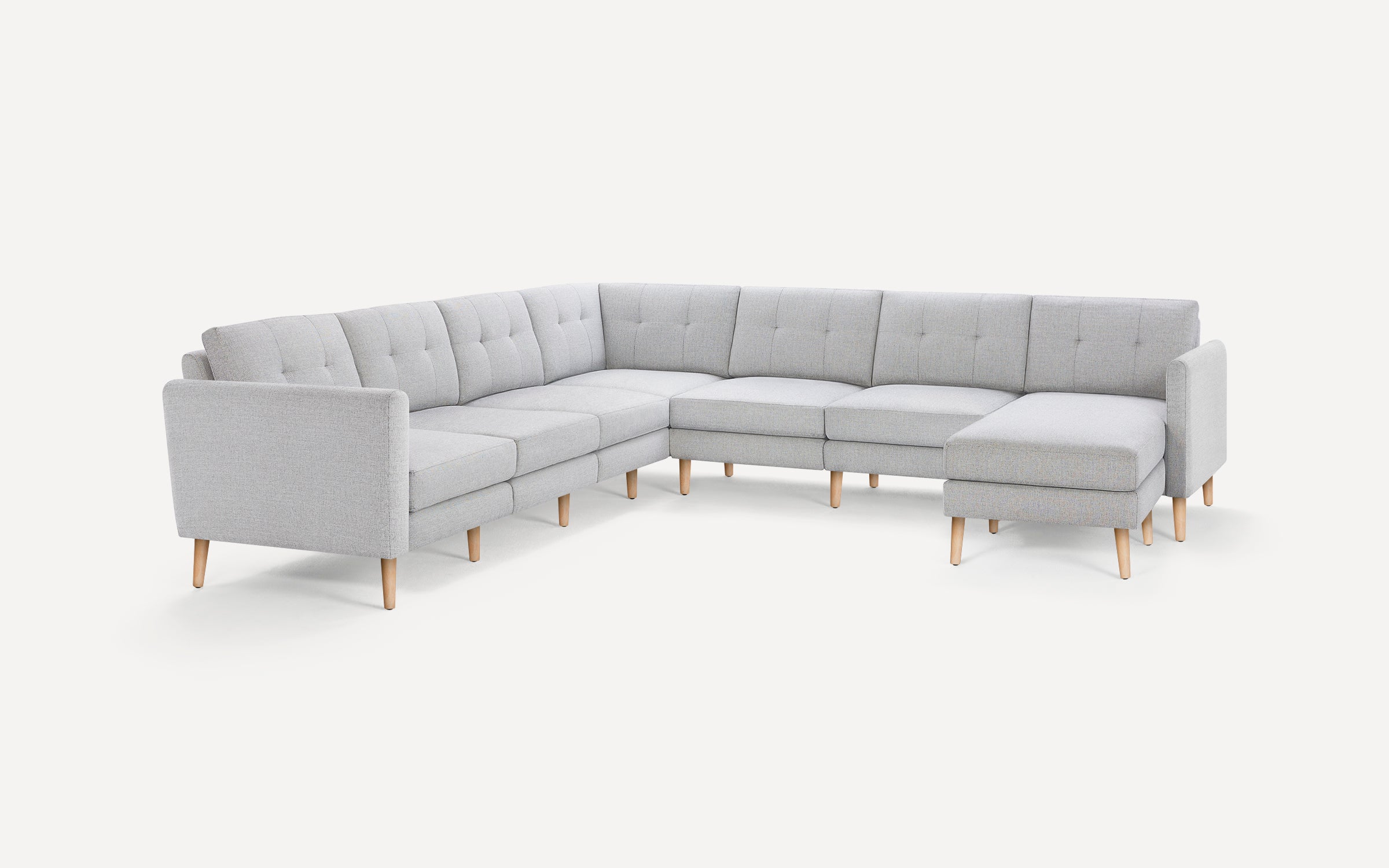 Light gray fabric upholstered sectional sofa with tufted back cushions and wooden legs, featuring a chaise lounge on the right side.