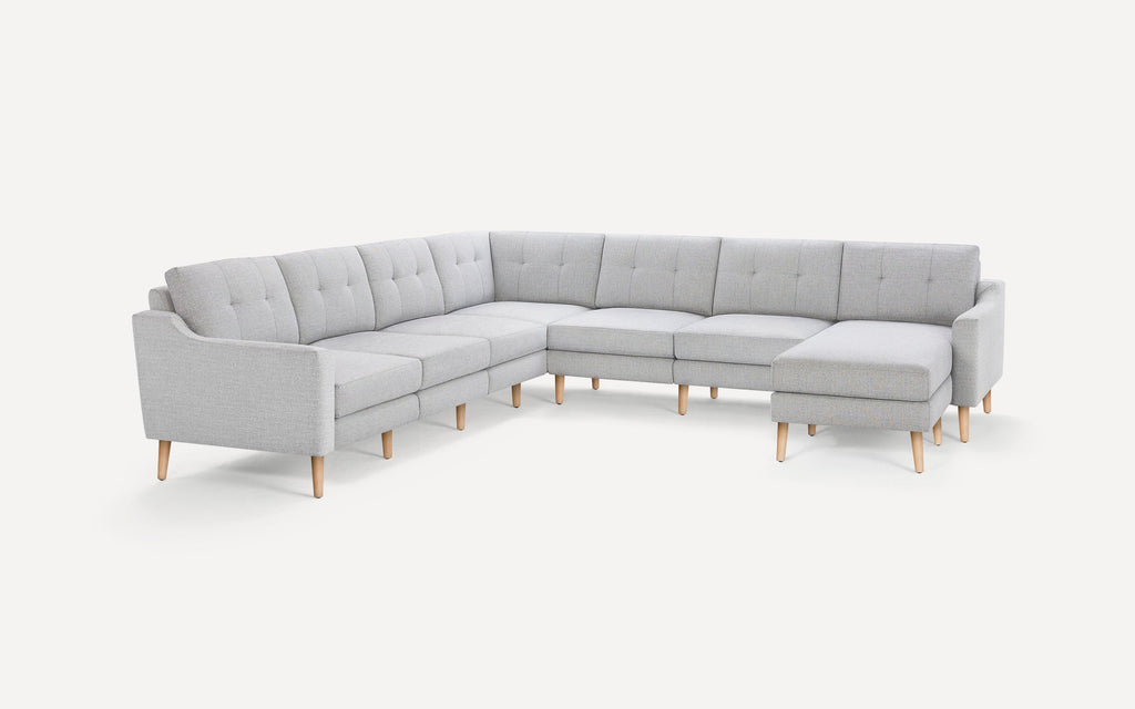 Modern light gray fabric sectional sofa with tufted backrests and wooden legs, arranged in an L-shape with a chaise lounge.