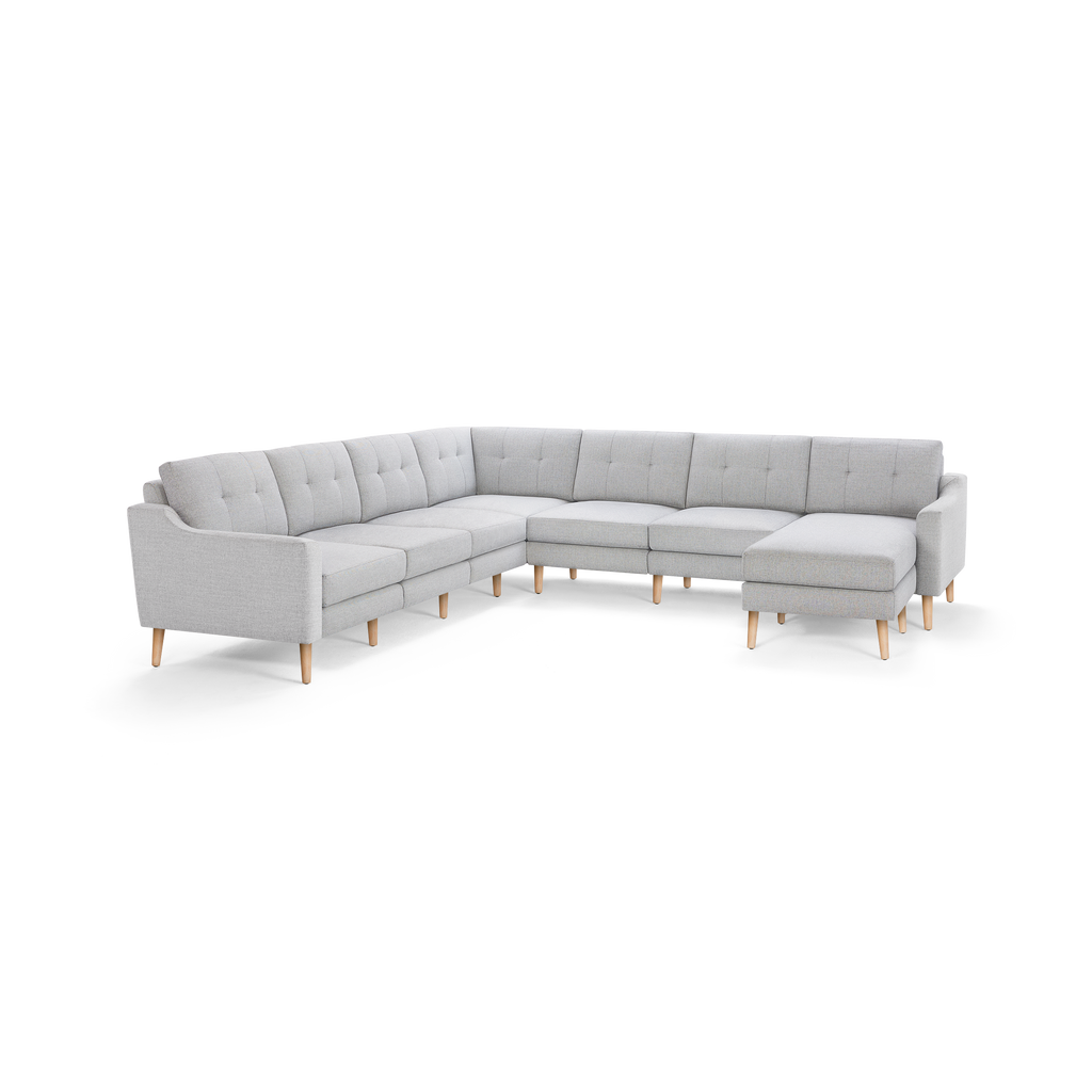Light gray fabric sectional sofa with tufted back cushions, wooden legs, and an L-shape design with a chaise lounge on the right side.