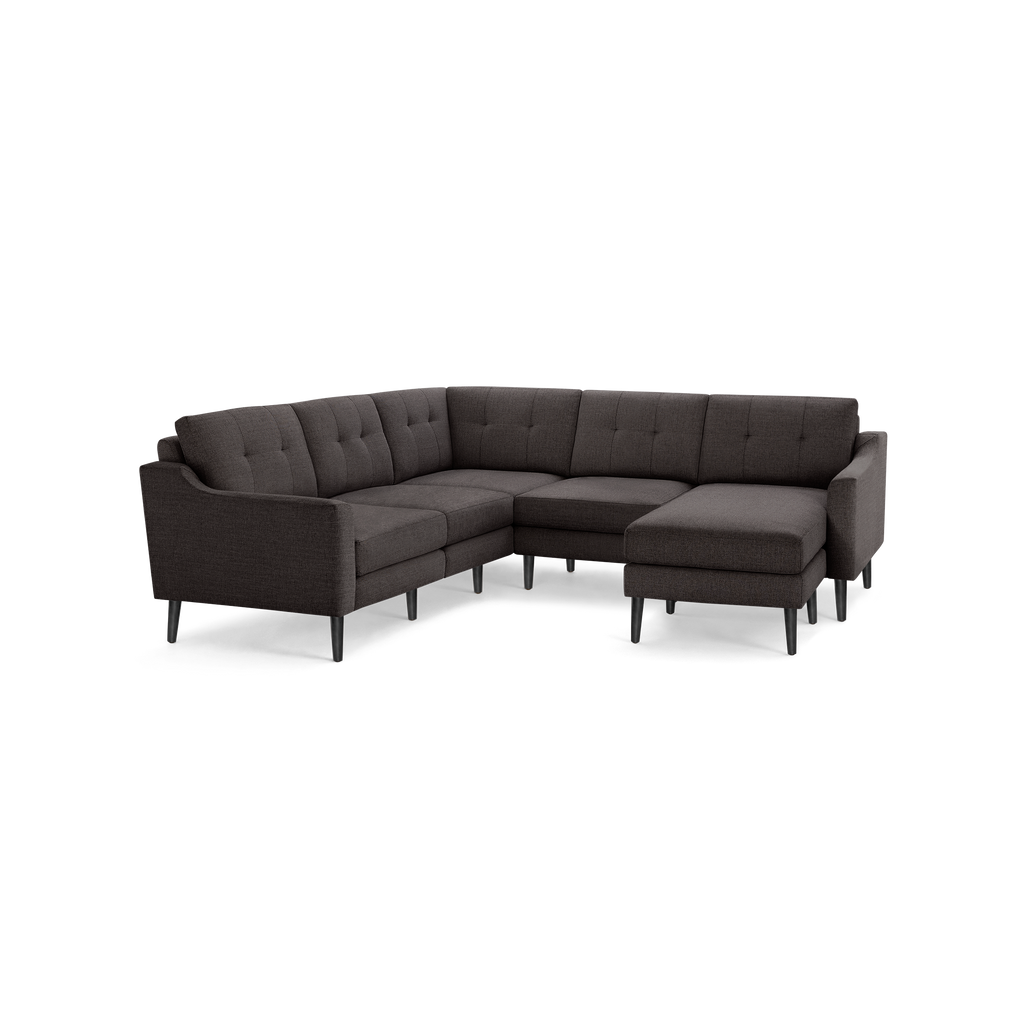 Dark gray upholstered fabric sectional sofa with tufted backrest, angled armrests, and slender black legs on black background.
