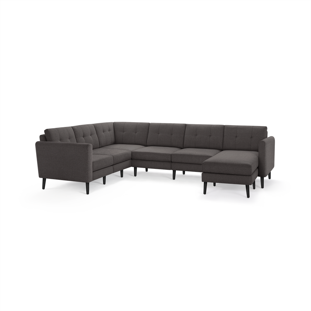 Dark grey L-shaped sectional sofa with tufted back cushions and slim black legs, featuring a chaise lounge on the right side.