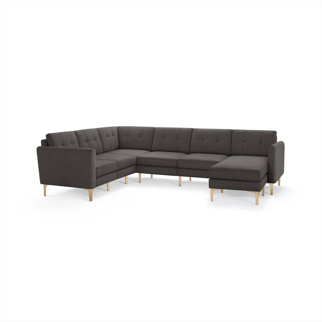 Dark gray L-shaped sectional sofa with tufted back cushions, slim armrests, and light wooden legs, isolated on white background.