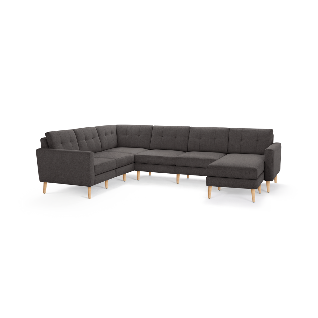 Dark gray upholstered L-shaped sectional sofa with tufted cushions and light wood tapered legs.