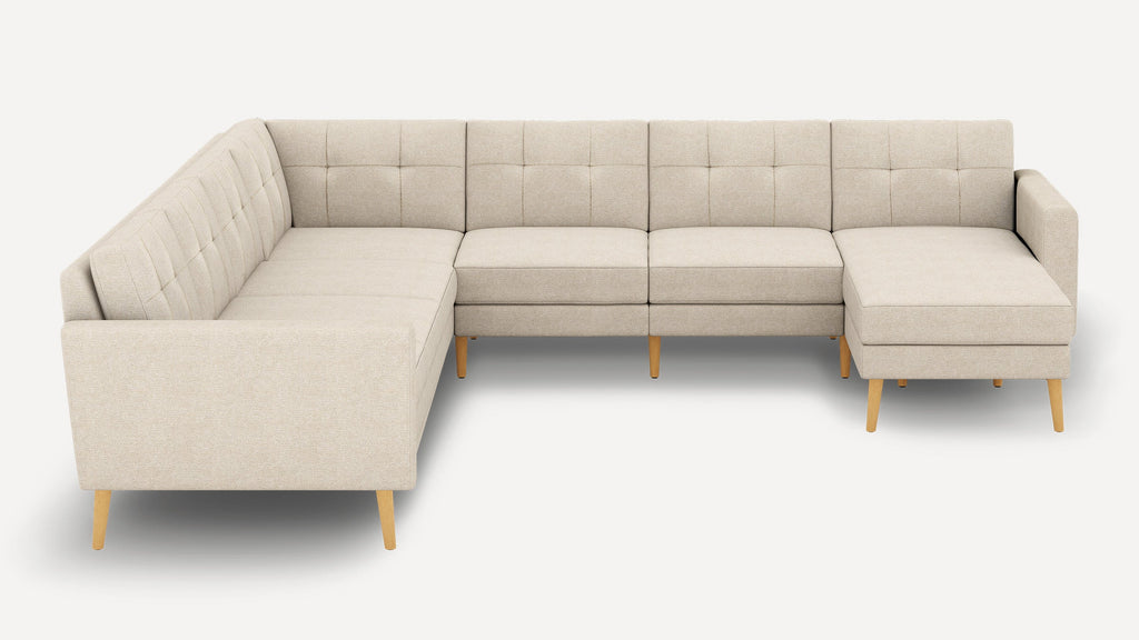 Beige fabric sectional sofa with tufted backrests, light wooden legs, and a chaise lounge on the right side.