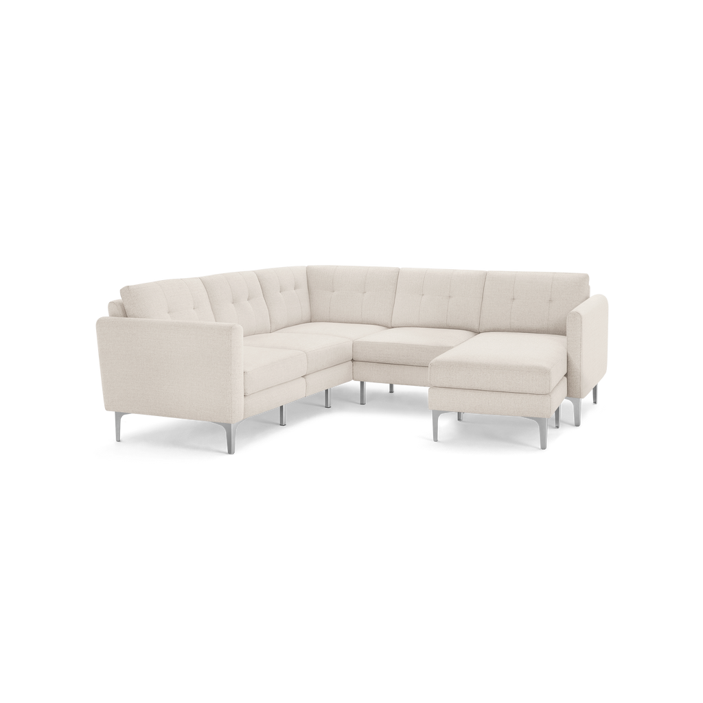 Modern L-shaped sectional sofa in light beige fabric with tufted back cushions and slim metal legs, featuring a chaise lounge on the right side.