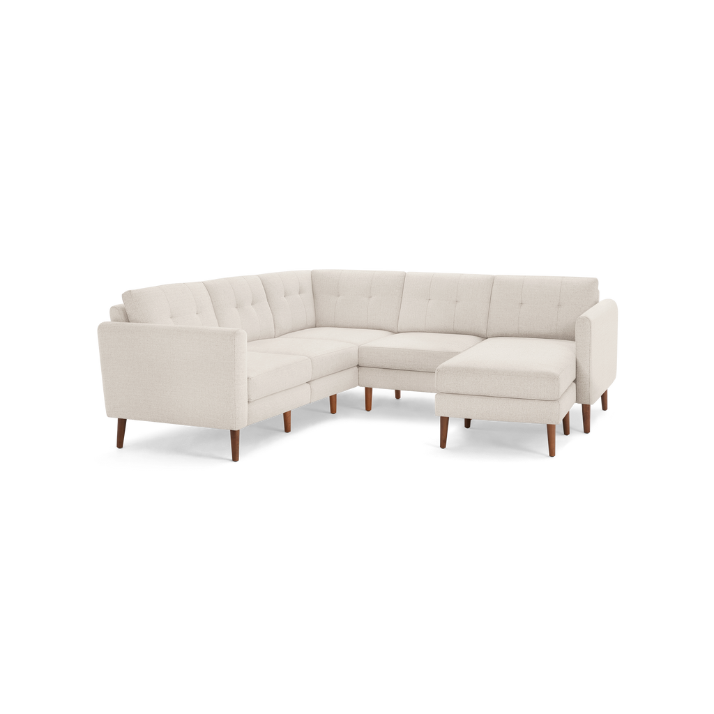 L-shaped beige fabric sectional sofa with tufted back cushions and wooden legs, featuring a chaise lounge on the right side.