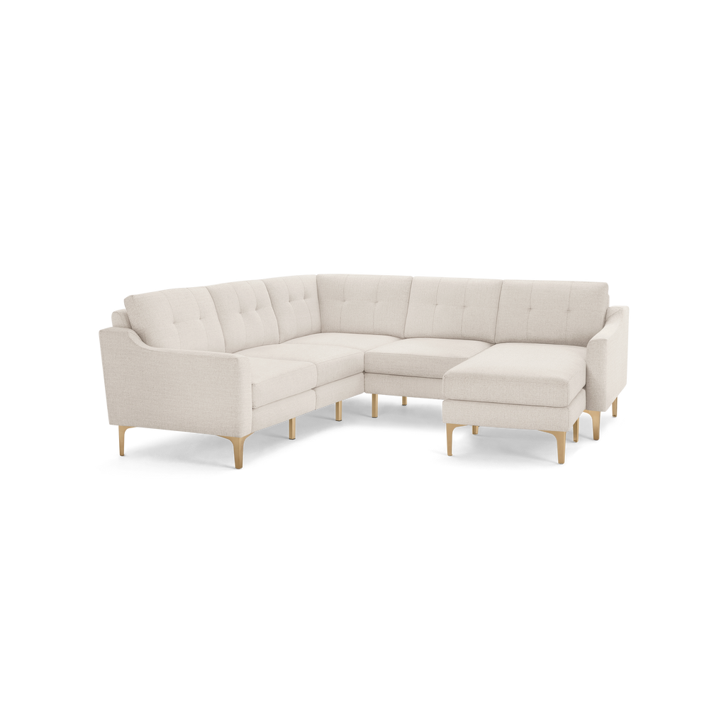 Modern L-shaped sectional sofa in light beige fabric with tufted back cushions and wooden legs on a black background.