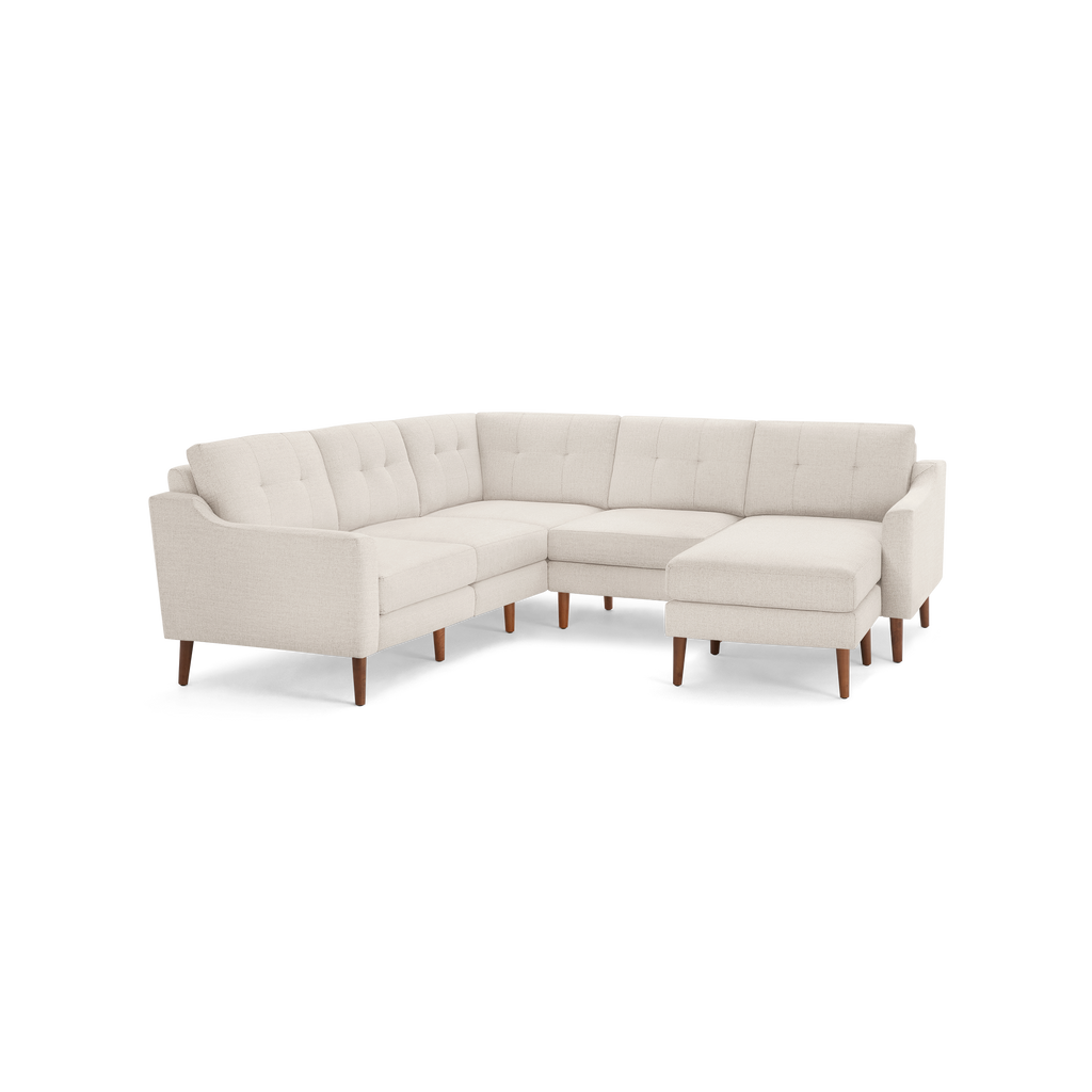 Light beige fabric sectional sofa with tufted back cushions, wooden legs, and an L-shaped design featuring a chaise lounge on the right side.