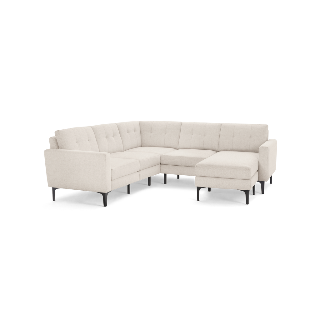 Light beige fabric L-shaped sectional sofa with tufted cushions and black angled legs on a black background.