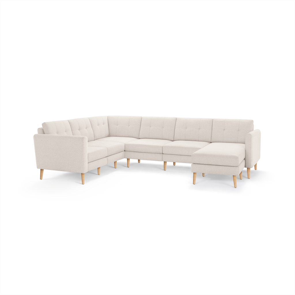 Beige L-shaped sectional sofa with tufted back cushions, wooden legs, and a chaise lounge on the right side.