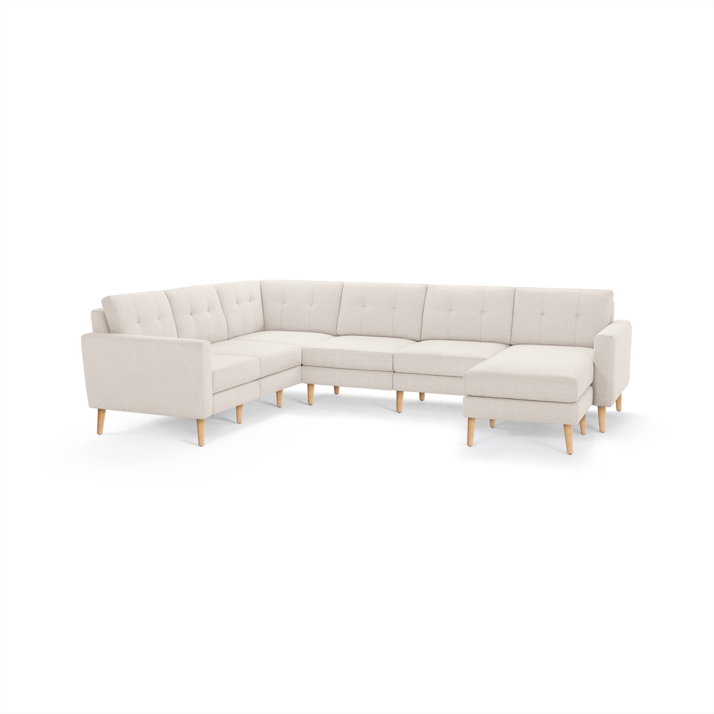 Beige fabric sectional sofa with tufted back cushions and wooden legs, featuring a right-side chaise lounge.