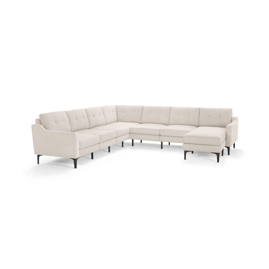 Large L-shaped beige sectional sofa with tufted back cushions and black slender legs, designed for spacious living rooms.