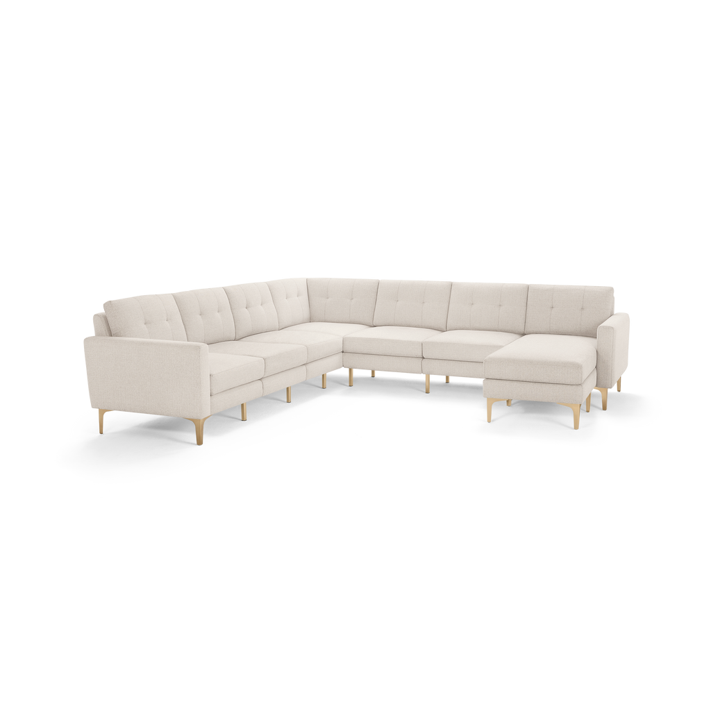 Large L-shaped sectional sofa with beige tufted fabric upholstery and light wooden legs, featuring a chaise lounge on the right side.