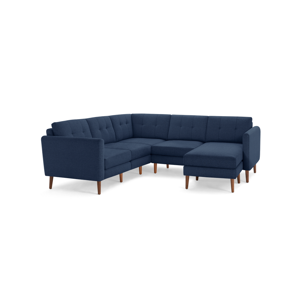 Large L-shaped sectional sofa in dark blue fabric with tufted cushions and tapered wooden legs.