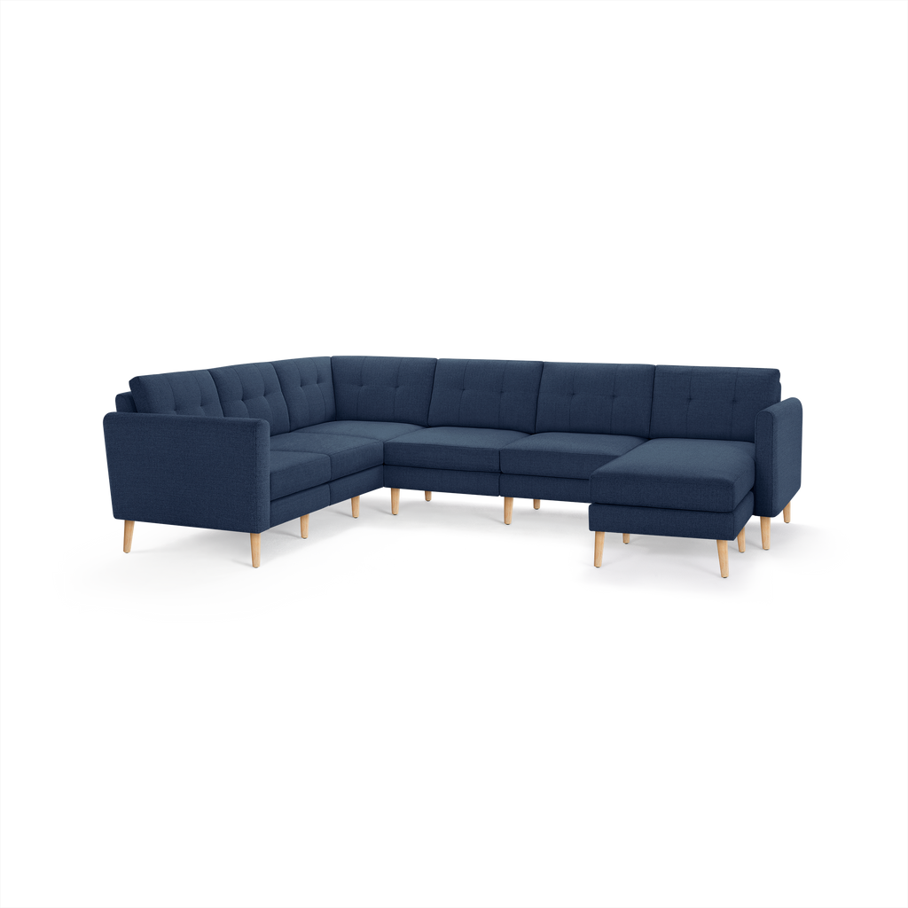 Large L-shaped sectional sofa upholstered in dark blue fabric with tufted back cushions and light wooden legs.
