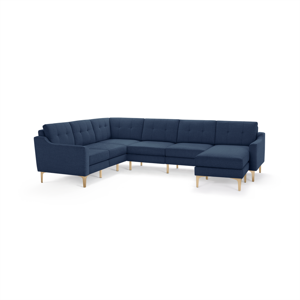 Large L-shaped sectional sofa in navy blue fabric with tufted back cushions and light wooden legs.