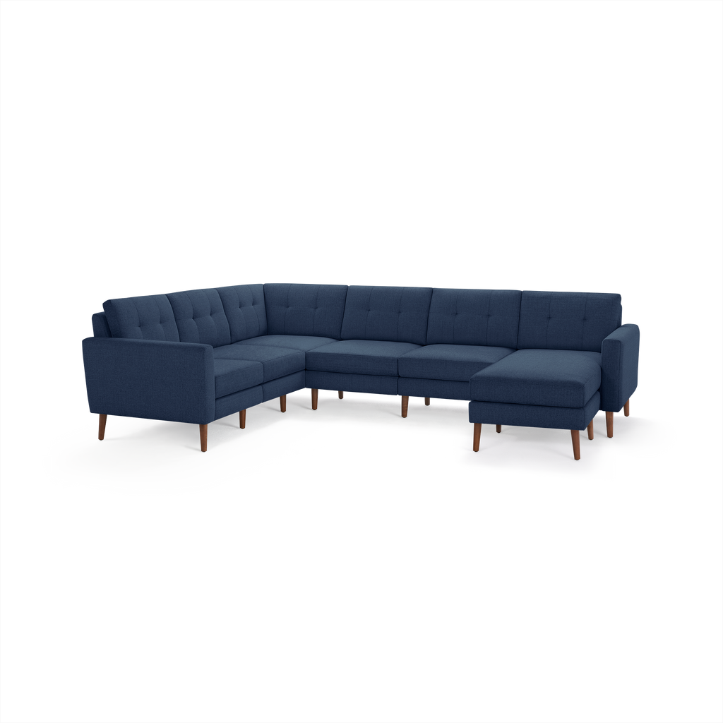 Large navy blue fabric sectional sofa with tufted cushions, wooden legs, and an L-shaped design with chaise lounge on the right side.