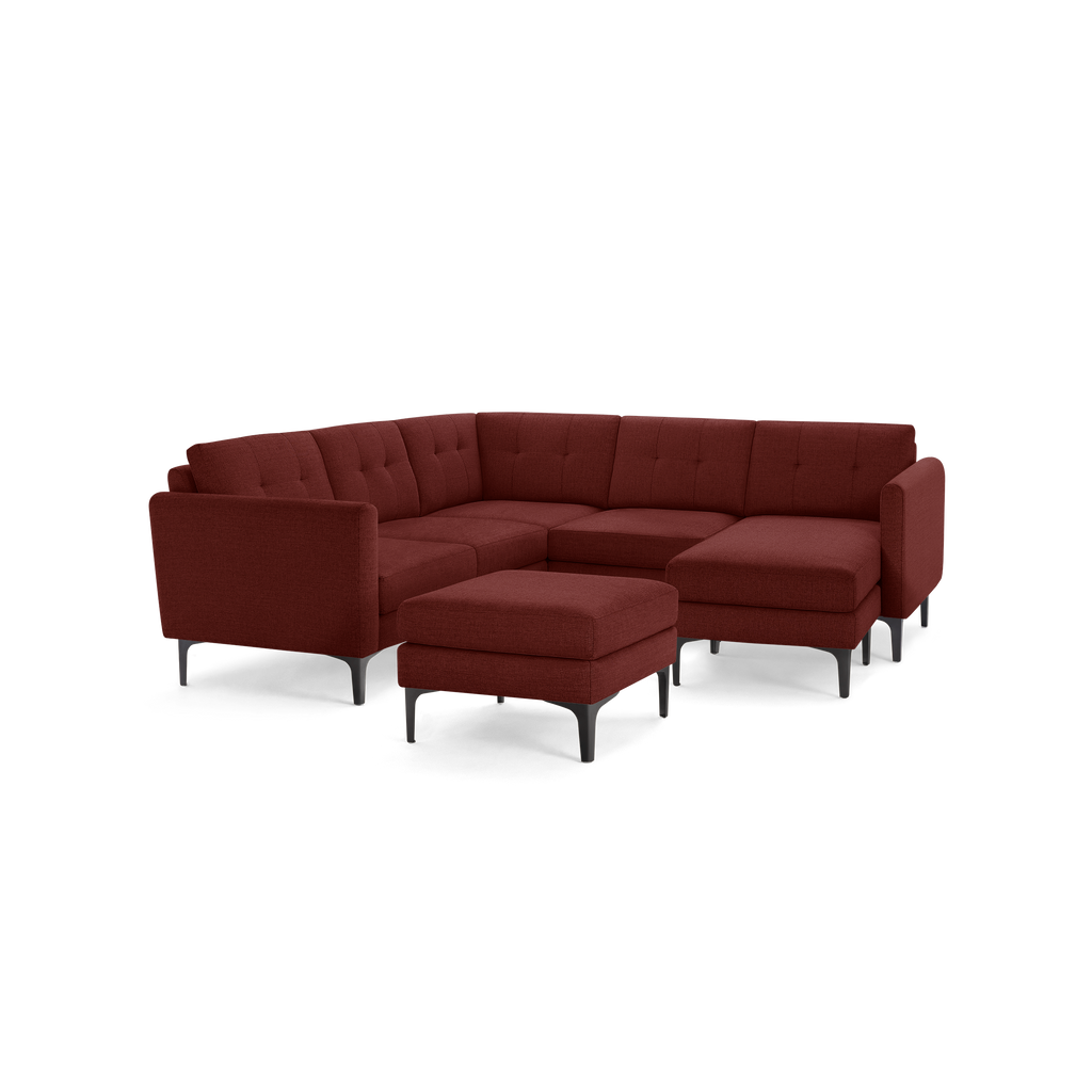 Modern L-shaped sectional sofa in deep red fabric with tufted cushions, slim black legs, and matching ottoman.