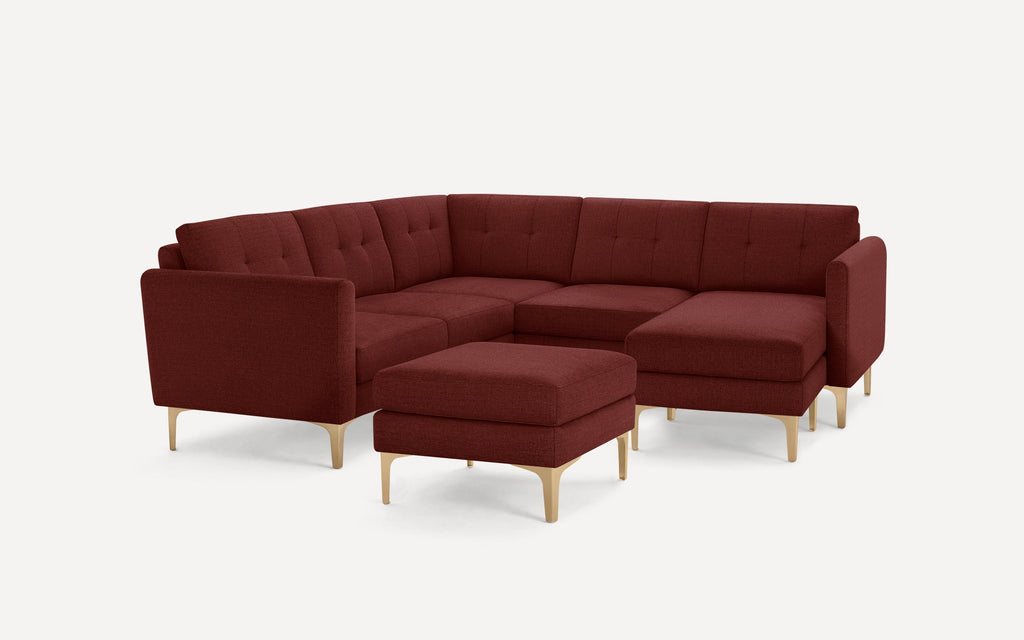 Modern deep red L-shaped sectional sofa with tufted back cushions, matching ottoman, and light wood tapered legs.