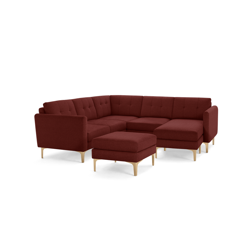Modern L-shaped sectional sofa in deep red fabric with tufted back cushions and light wooden legs, including a matching ottoman.