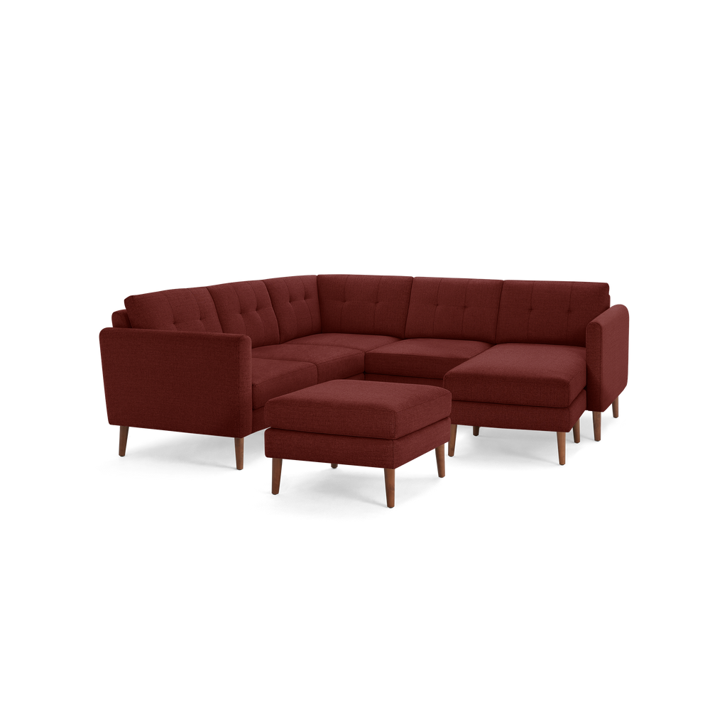 Modern L-shaped sectional sofa in deep red fabric with tufted cushions and matching ottoman on wooden legs.