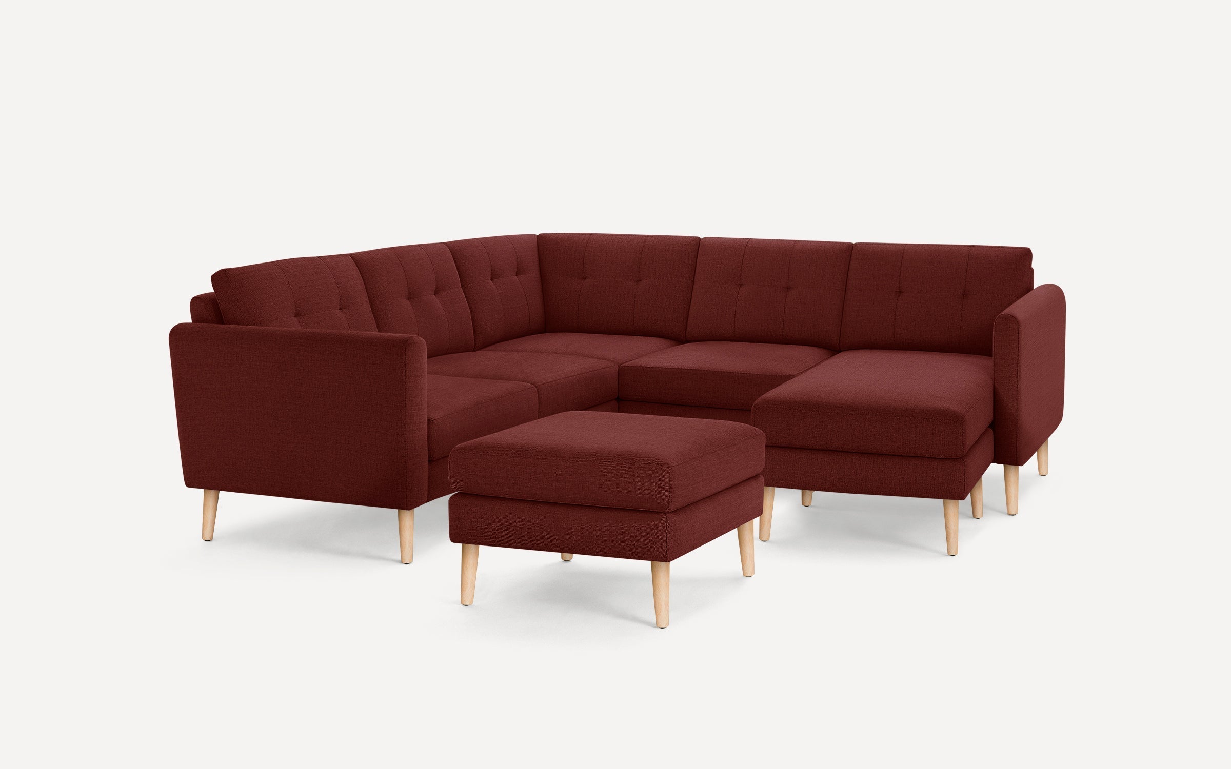 Modern burgundy fabric sectional sofa with tufted backrests and light wooden legs, including a matching upholstered ottoman.