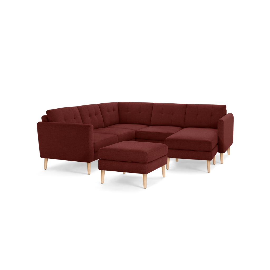 Modern L-shaped sectional sofa with deep red fabric upholstery, tufted back cushions, and light wooden legs, including a matching ottoman.