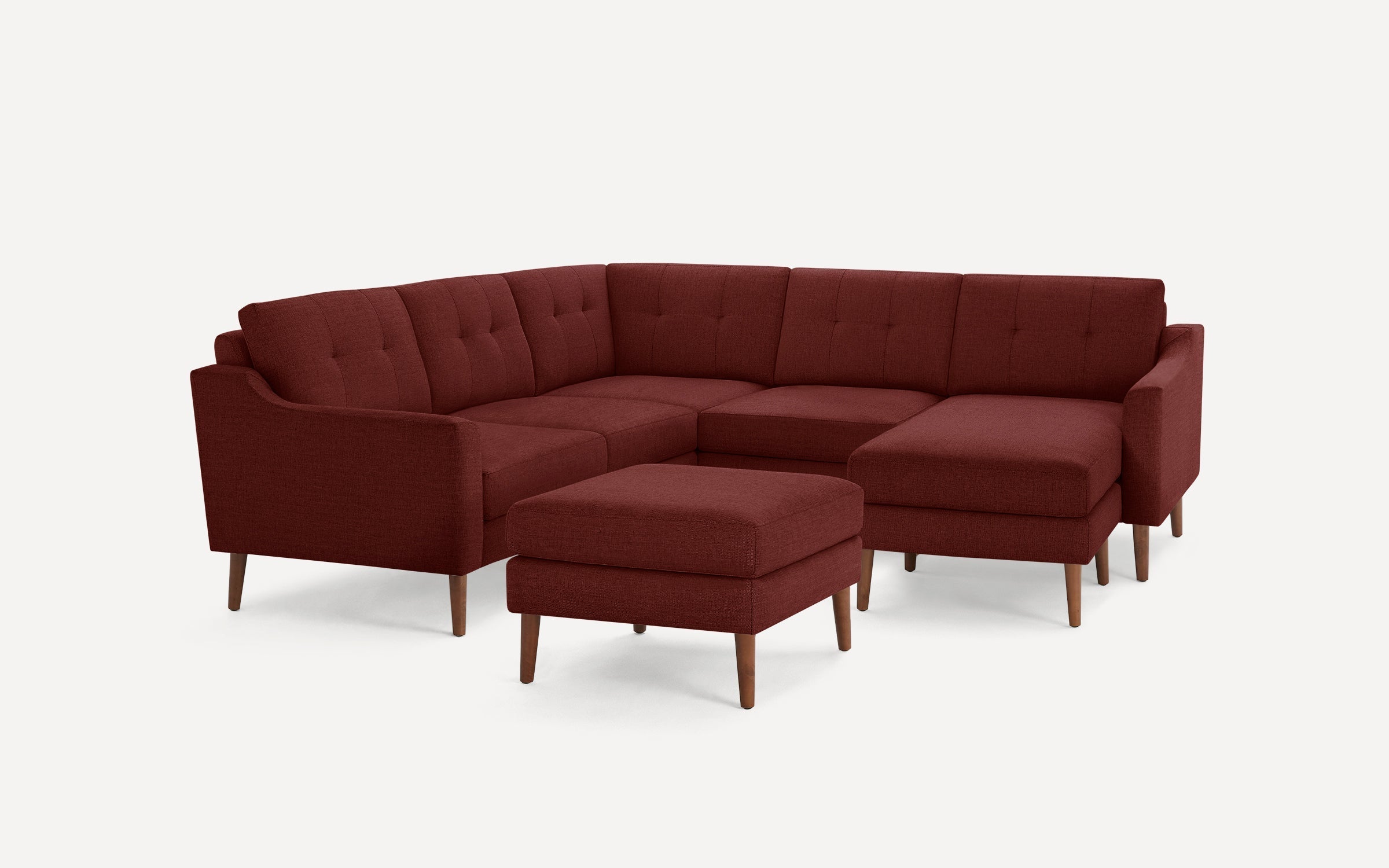 Modern L-shaped sectional sofa in deep burgundy fabric with tufted cushions and wooden tapered legs, including a matching ottoman.