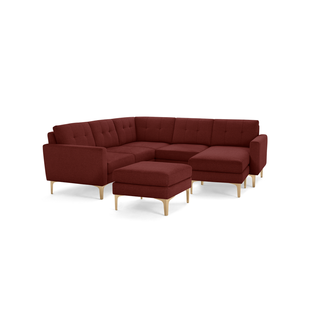 Modern L-shaped sectional sofa with tufted back cushions and matching ottoman in rich burgundy fabric, supported by light wooden legs.