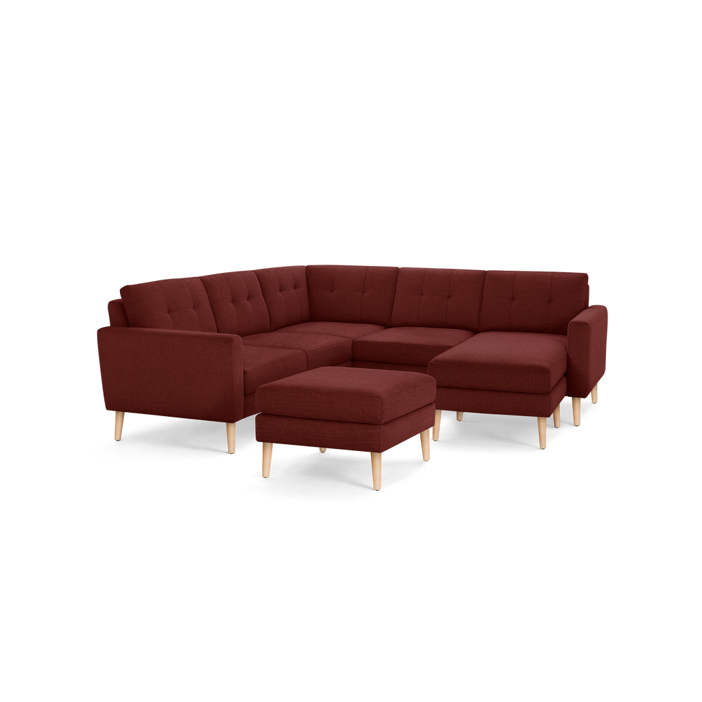 Modern L-shaped sectional sofa in deep burgundy fabric with tufted back cushions and light wooden legs, includes matching ottoman.